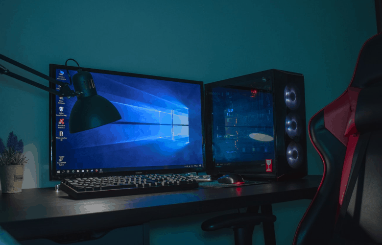 A picture of a monitor and a cpu on top of a desk with a gaming chair infront