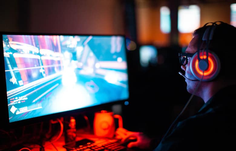 Guy wearing gaming headphones in-front of a monitor playing games